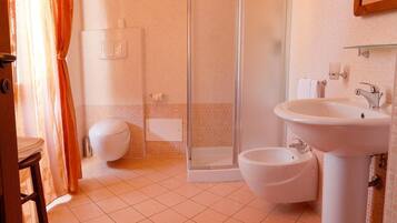 A bathroom with a shower, toilet, bidet, and sink.