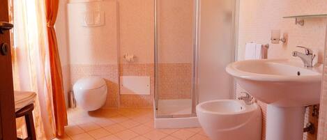 A bathroom with a shower, toilet, bidet, and sink.
