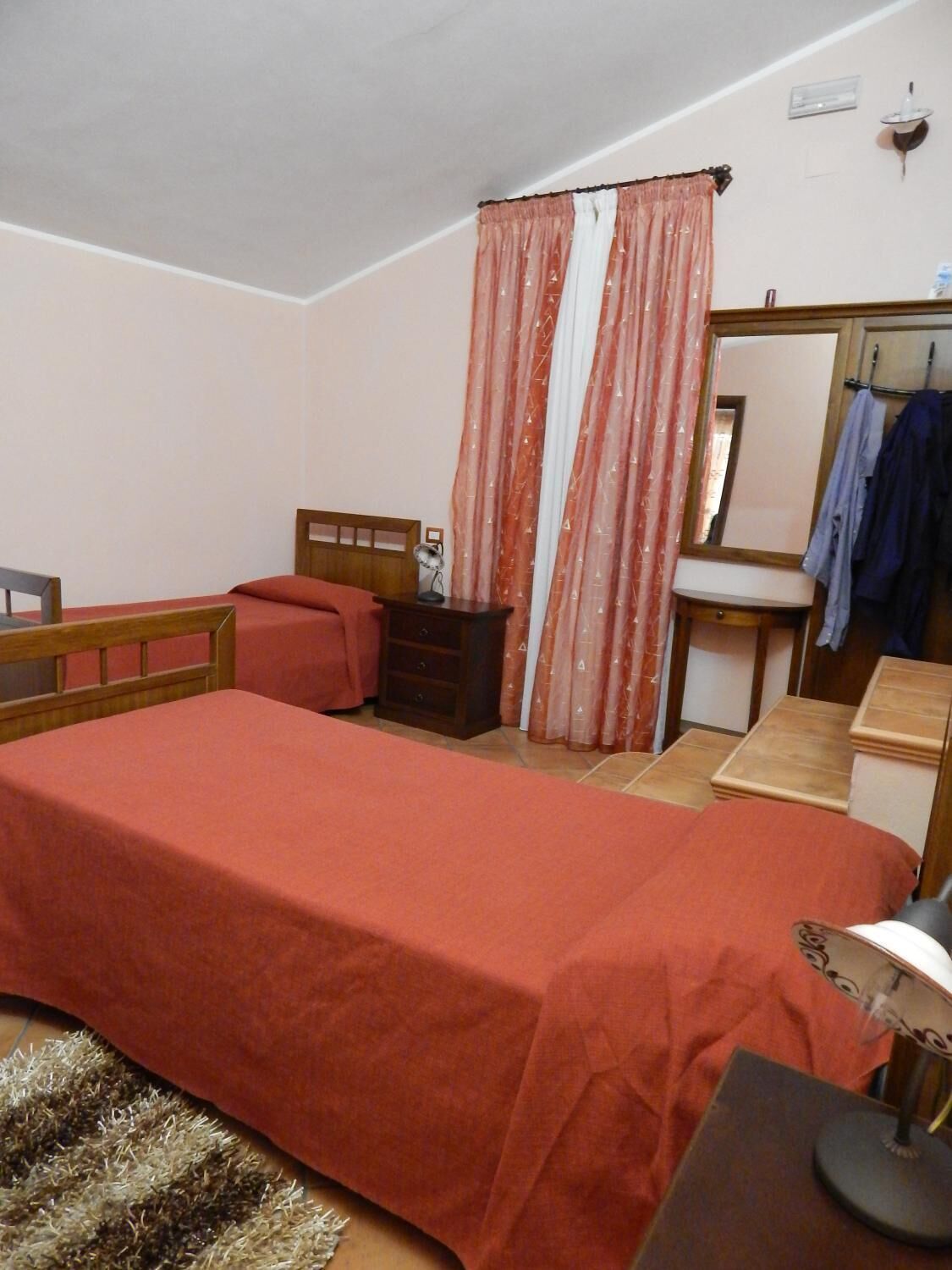 Une chambre avec un lit simple, une table de chevet avec une lampe, un miroir, une petite commode et une chaise.