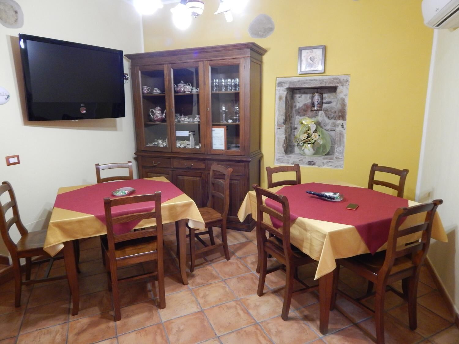 Un comedor con dos mesas, sillas de madera, un televisor, un mueble bar con puertas de vidrio y una chimenea de piedra.