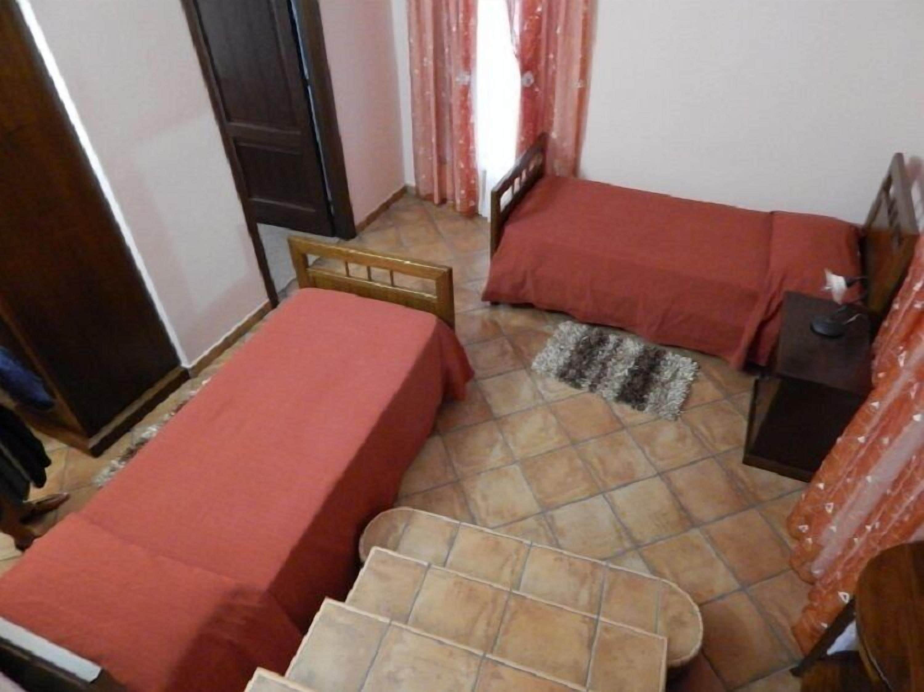 A small, compact room with two single beds, a small table, and a wardrobe.