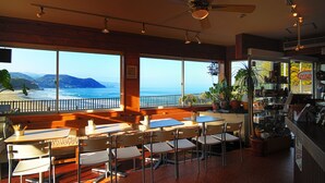 Un restaurante con vista al océano, mesas, sillas y una zona de bar.