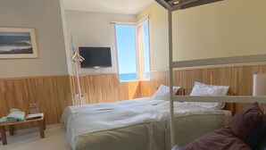 Habitación de hotel con cama, banco, televisión y ventana con vista al mar.