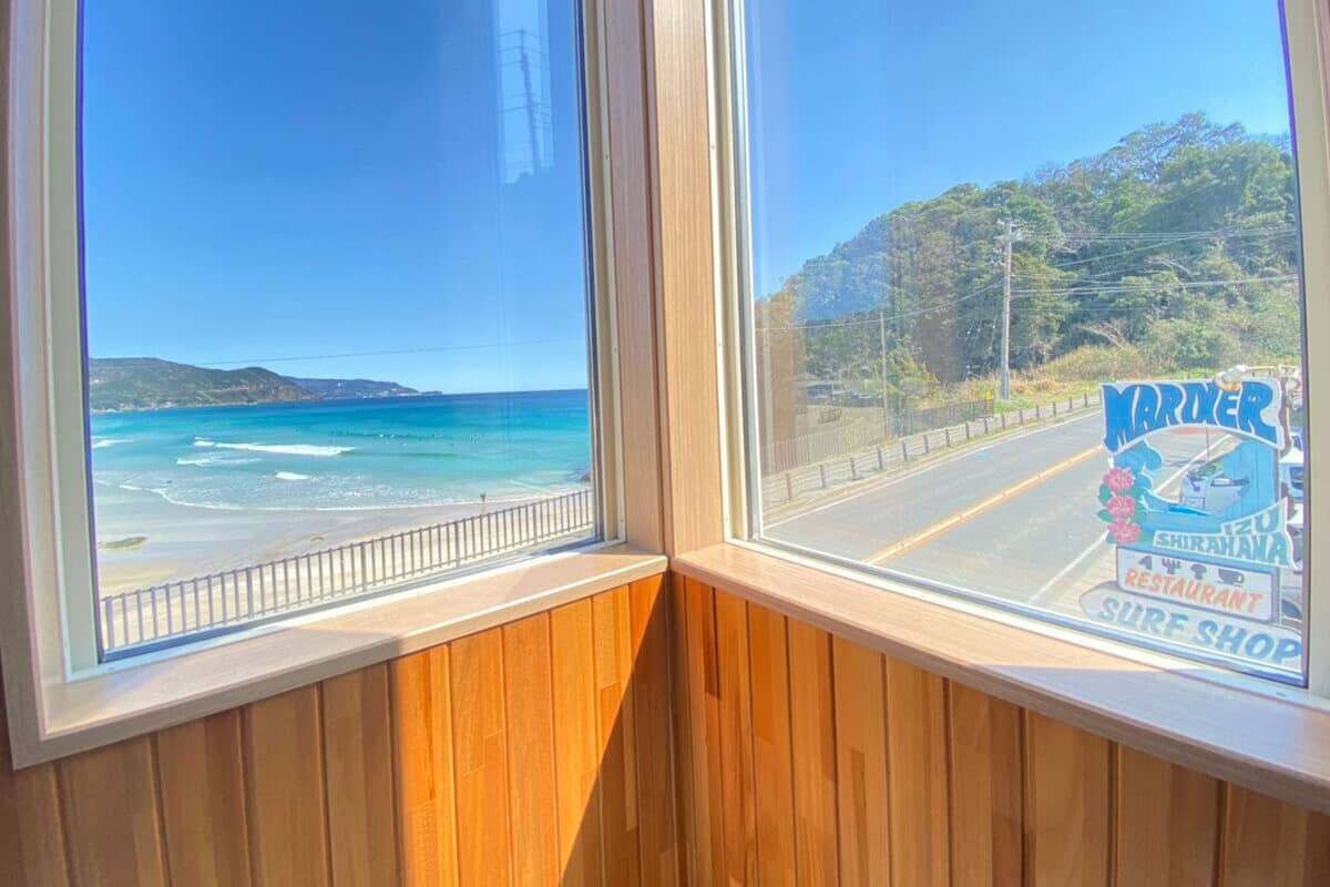 A view of a beach through a window with a wooden frame.