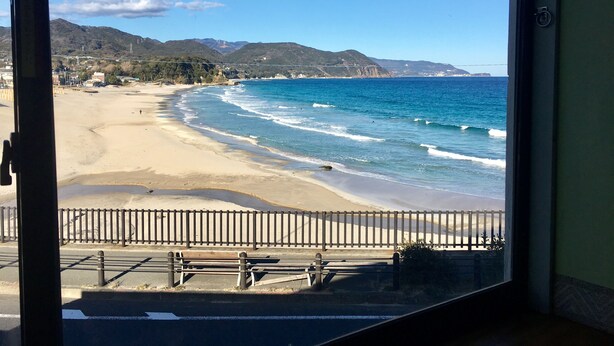 Vista de la playa desde el interior de un edificio, con un banco de madera y una valla de metal al frente.