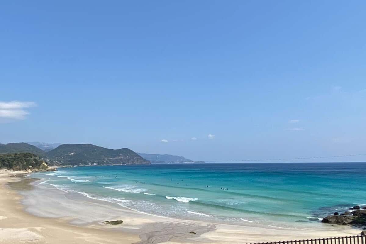 A beach with clear turquoise waters, sandy shore, and distant mountains.