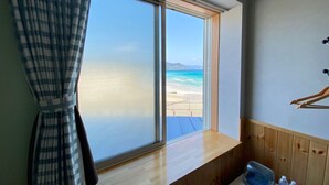 Habitación con un amplio ventanal con vista a la playa, paneles de madera, una pequeña mesa con una botella de agua y un perchero.