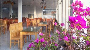 Ein Restaurant mit Holztischen und -stühlen, hängenden Korblampen und einem Fahrrad im Hintergrund.