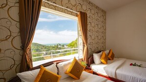 Ein Hotelzimmer mit zwei Betten, einem großen Fenster mit Vorhängen, strukturiertem Wandpapier und Blick auf Grünflächen und Gebäude.