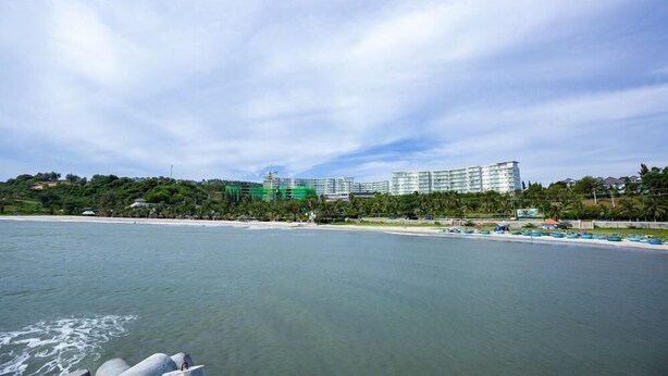 Ein Hotel an der Küste mit Blick auf den Strand, mehreren Etagen und einem großen Gebäude im Hintergrund.