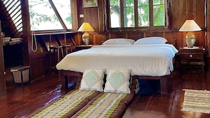 Un dormitorio de madera con una cama grande, dos lámparas de noche y vistas a zonas verdes a través de las ventanas.