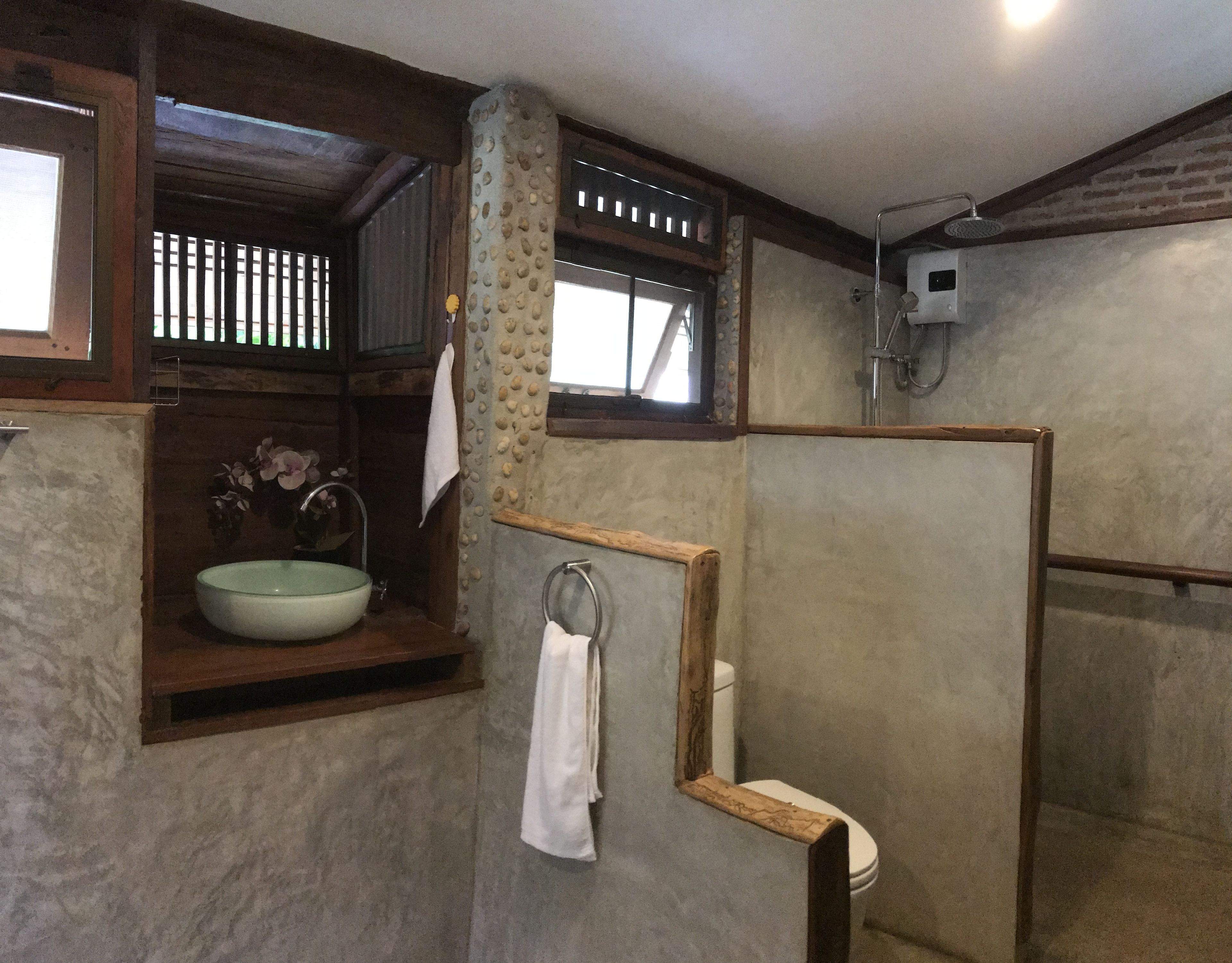 Een badkamer met een stenen wastafel, houten planken, een toilet en een douchehoek.