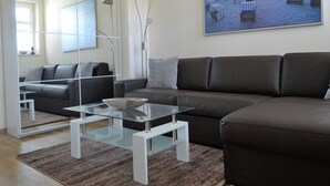 A modern living room with a brown leather sofa, a glass coffee table, and a large painting of beach chairs on the wall. - 3-room vacation apartment Villa Parkblick, 55 inch UHD, Blu-ray, renovated in 2024 (Kühlungsborn Ost)