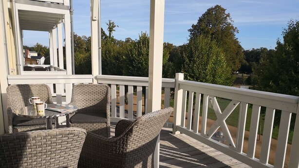 A covered outdoor seating area with wicker furniture and a table, overlooking a landscaped garden and trees. - 3-room vacation apartment Villa Parkblick, 55 inch UHD, Blu-ray, renovated in 2024 (Kühlungsborn Ost)