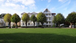 A multi-story residential building with a balcony, surrounded by a well-maintained lawn and trees. - 3-room vacation apartment Villa Parkblick, 55 inch UHD, Blu-ray, renovated in 2024 (Kühlungsborn Ost)