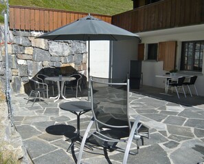 Un patio al aire libre con piso de piedra, mesas y sillas de metal, una chimenea de piedra y una valla de madera.