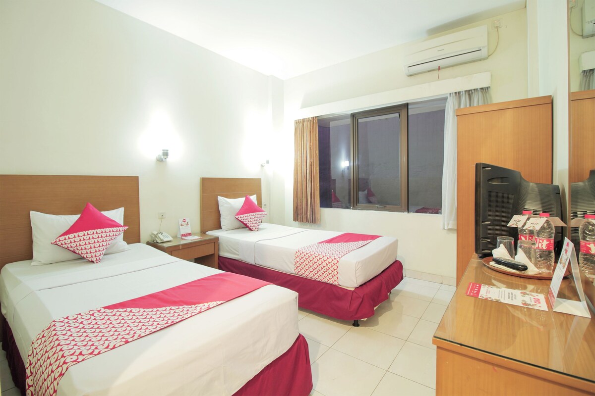 Quarto de hotel com duas camas, uma escrivaninha e uma janela.