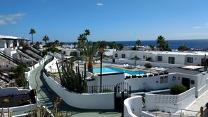 Zona de piscina en la azotea con vista despejada al océano, rodeada de edificios blancos y palmeras.