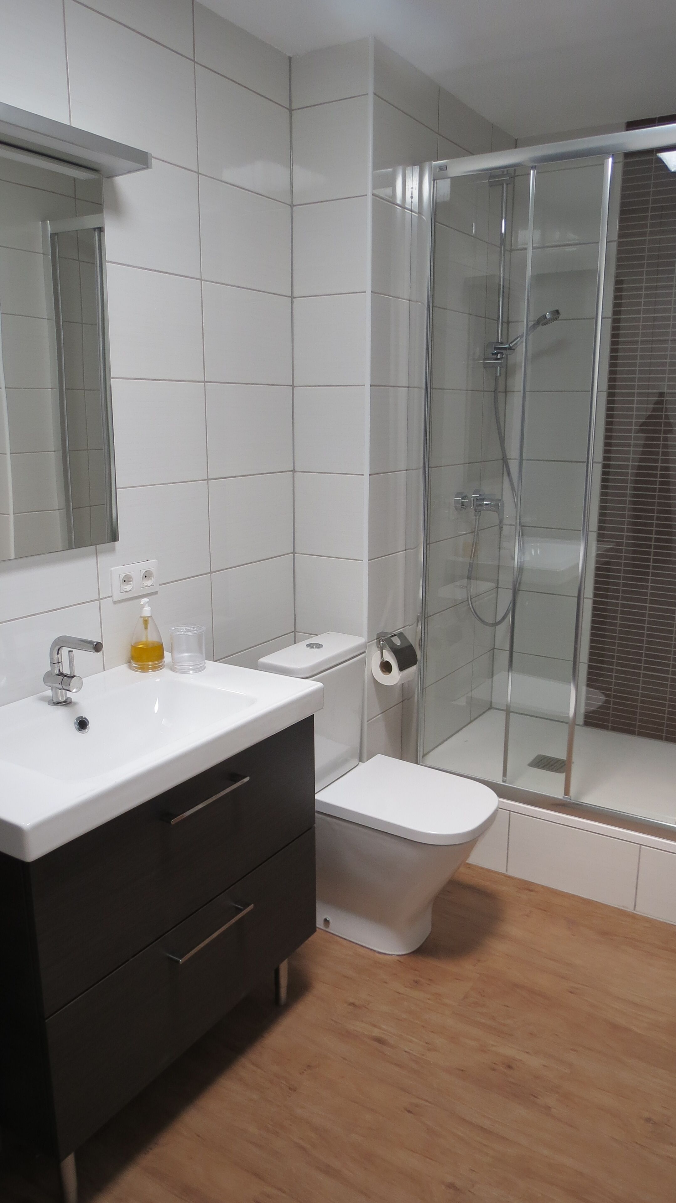 Ein modernes Badezimmer mit Waschbecken, dunklem Unterschrank, Toilette und Duschkabine aus Glas.