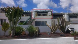Un edificio con un área exterior techada, varios cactus y una escalera que lleva a un nivel superior.