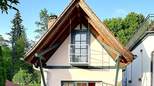 Une maison à deux étages, dotée d’un toit en pente, de grandes fenêtres et d’une terrasse aménagée avec du mobilier d’extérieur.