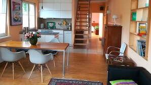 Une cuisine moderne avec des meubles blancs, un coin repas doté d’une table et de chaises en bois, et un escalier menant à un autre niveau.