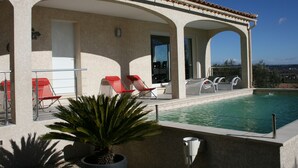 Zona junto a la piscina con sillas de descanso rojas, una planta en maceta y vista despejada del estanque.