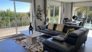 Una sala de estar moderna con un sofá de cuero, una mesita de centro y vistas al exterior a través de amplios ventanales.