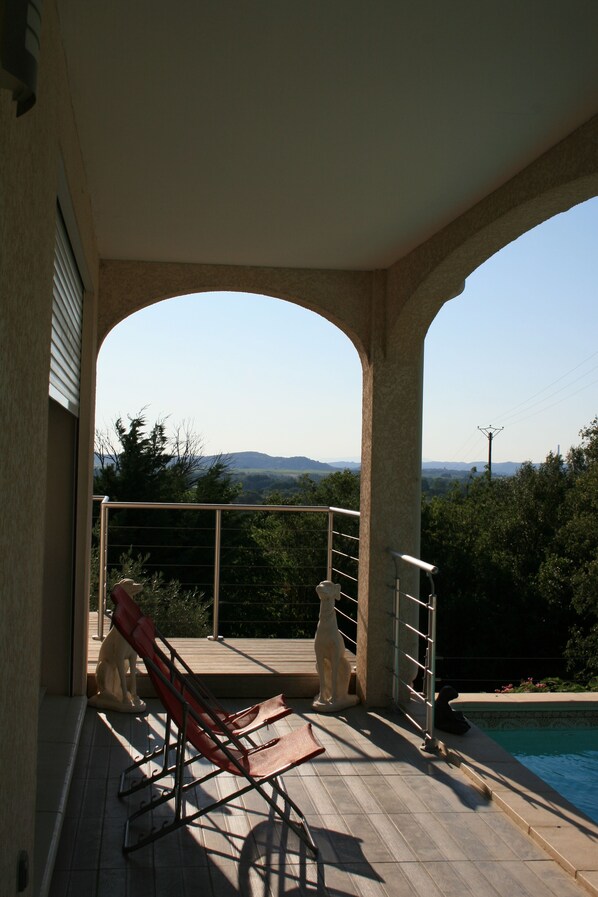 A covered outdoor area with a pool, a red lounge chair, and two white statues. - Villa with swimming pool, bowling green and panoramic view (Sernhac)