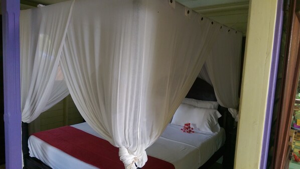 Una cama con ropa de cama blanca y una manta roja, un dosel blanco y una pequeña decoración de flor roja.