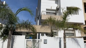 A modern multi-story building with white exterior walls, a gated entrance, and palm trees. - At the heart of Rabat Beaches (Harhoura)