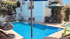 A swimming pool with lounge chairs and umbrellas, surrounded by a white building with a tiled floor. - At the heart of Rabat Beaches (Harhoura)