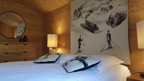 Ein Zimmer aus Holz mit einem Bett, einem Schminktisch, einem Spiegel, einer Lampe und einem großen Wandbild von Skifahrern.
