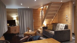Ein gemütliches Wohnzimmer mit einer Holztreppe, einem Fernseher und einem Sofa.