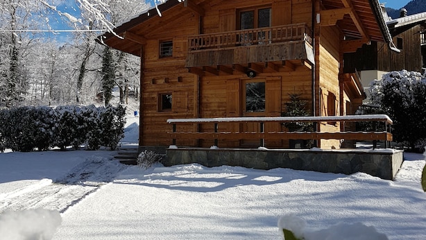 Eine Holzhütte mit Balkon, umgeben von schneebedeckten Bäumen und wolkenlosem, blauem Himmel.