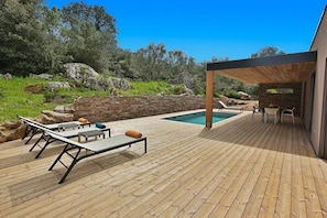 Eine Holzterrasse mit Pool, Sitzgelegenheiten im Freien und einer Steinmauer.
