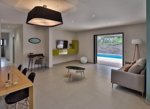 Ein modernes Wohnzimmer mit Essbereich, Fernseher und Blick auf ein Außen-Schwimmbad.
