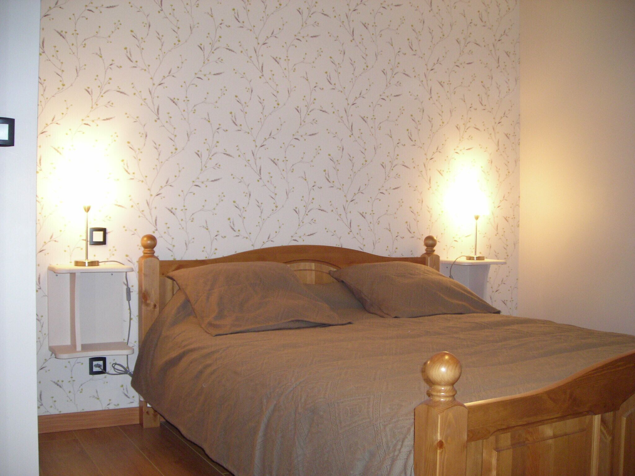 A bed with a wooden headboard, two bedside lamps, and a floral wallpaper pattern.