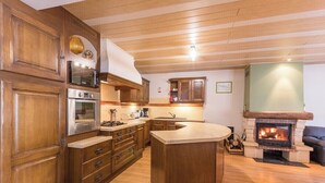 A kitchen with wooden cabinets, a central island, a built-in oven, a microwave, and a fireplace. - Gîte du Champ Chequelin - 3 ears 4 stars (Corravillers)