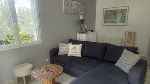 A modern living room with a grey sectional sofa, a round wooden coffee table, a small round ottoman, a white radiator, and a ceiling light fixture. - Quiet, 3-star rated house, 800m from beaches and coastal paths (Tregunc)