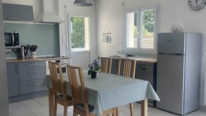 A compact kitchen with a dining table, chairs, a refrigerator, and a clock on the wall. - Quiet, 3-star rated house, 800m from beaches and coastal paths (Tregunc)