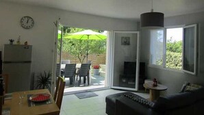 A living room with a sofa, a dining table with chairs, a TV, and a sliding glass door leading to an outdoor patio with a table and chairs. - Quiet, 3-star rated house, 800m from beaches and coastal paths (Tregunc)