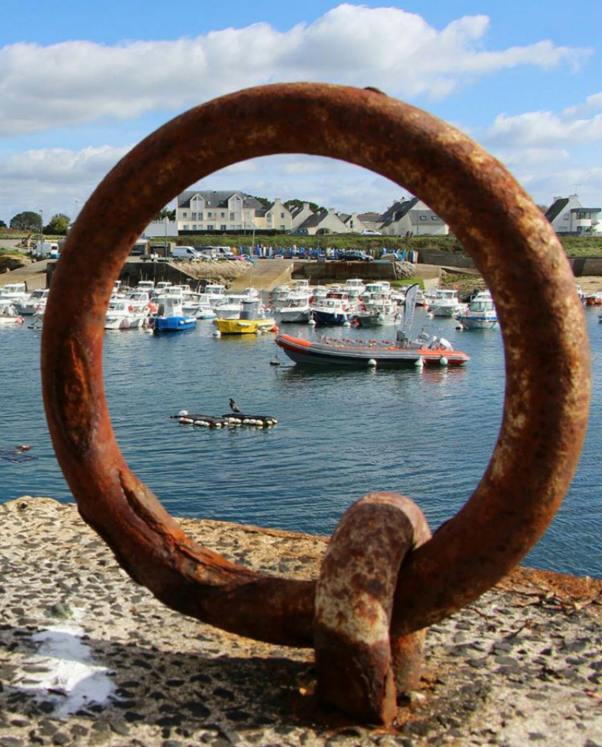 A rusty metal ring in the foreground with a marina and boats in the background.