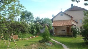 Ein Haus mit einem Ziegeldach, einer Holzveranda und einem Garten mit Schaukel.