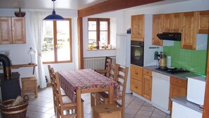 Eine Küche mit Holzausstattung, einem Esstisch mit Stühlen, einem Herd und einem Fenster.