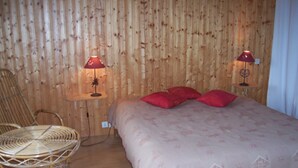 Ein Zimmer mit einem Bett, zwei roten Lampen, einem Korbsessel und einem kleinen Tisch.