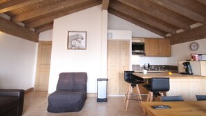 Un'accogliente zona giorno con divano, tavolo da pranzo e cucina con pensili in legno e orologio.
