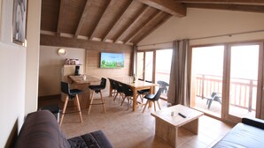 Un accogliente soggiorno con divano, tavolino da caffè e zona pranzo con sedie e tavolo. C'è una TV montata a parete e un balcone con vista.