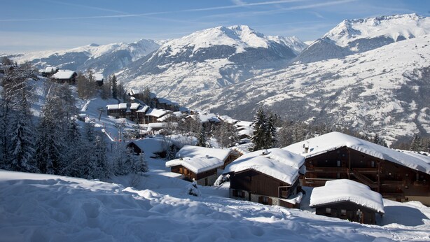 Un villaggio innevato tra le montagne, con caratteristiche case di legno e vista libera sulle cime circostanti.