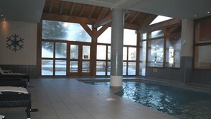 Una piscina interna con ampie vetrate, travi in legno e pavimento piastrellato.